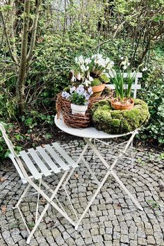 an outdoor table and chair covered in moss with flowers on it next to some trees