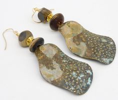 1 Pair Available! Pics do not do justice....long wavy handforged brass drops have been textured with hammer and patinated.  Raised dots are brushed to reveal shiny gold metal..  The colors are subtle....a little speck of blue, some golden tan, gray-blue, dark brownlovely patterns created by patination.  I have topped the statement sized drops with stack of handcarved horn beads separated by GP  bead. Earrings are a tad over 3 1/2 inches in length, including my handmade 14KT GF French wires.  Lig Earthy Bronze Brass Earrings, Rustic Gold Drop Earrings, Artistic Gold Earrings With Patina, Rustic Brass Earrings With Patina, Rustic Gold Brass Earrings, Rustic Gold Metal Earrings, Artisan Brass Earrings With Patina, Hand Forged Brass Earrings In Brown, Rustic Gold Dangle Jewelry