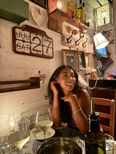 a woman sitting at a table with wine glasses and plates on the wall behind her