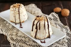 two desserts on a white plate with chocolate drizzled over them and walnuts in the background