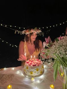 two women sitting at a table with a cake and flowers in front of them,