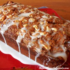 a loaf of cake with icing and nuts on top sitting on a red plate