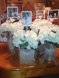 white flowers in vases sitting on a table with pictures and frames behind them,