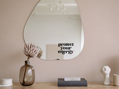 a mirror that says protect your energy next to a vase with a flower in it