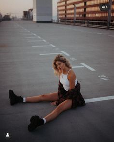 a woman sitting on the ground with her legs crossed and wearing tennis shoes in front of an empty parking lot