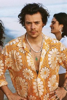 a man in an orange shirt standing next to the ocean with his hands on his hips