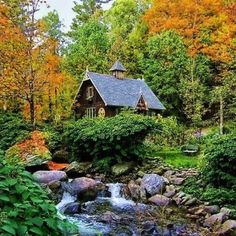 a house in the woods surrounded by rocks and trees with fall foliage around it, near a stream