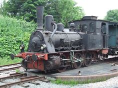 an old black train engine sitting on the tracks next to some grass and trees in the background