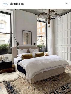 a bedroom with a large bed and lots of pillows on the floor next to two windows