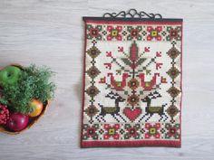 a bowl of fruit sitting next to a cross stitch wall hanging on a wooden table