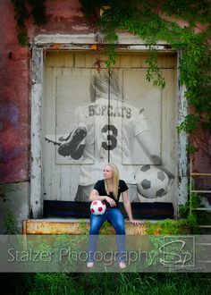 a woman sitting on a bench holding a soccer ball in front of a wall with graffiti