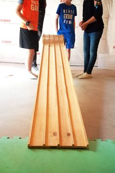 three people are standing in front of a wooden slatted board that is laying on the floor