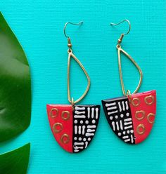 a pair of red and black earrings sitting on top of a green leafy plant