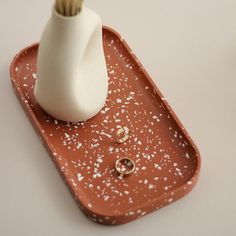 an orange tray with two rings and a white vase sitting on top of the tray