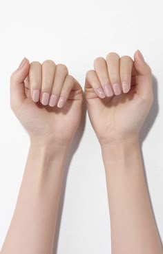 two hands with pink manicures holding up their fingers against a white wall background