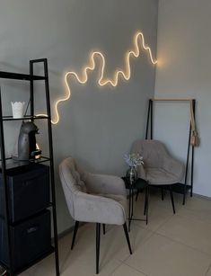 two chairs and a table in a room with lights on the wall behind them,