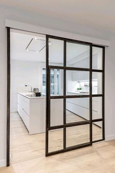 an open kitchen with white cabinets and wood floors is reflected in the glass door on the wall