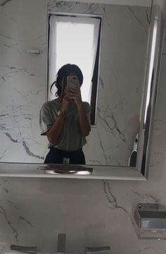 a woman taking a selfie in front of a bathroom mirror with her cell phone