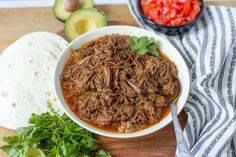 shredded meat in a bowl with cilantro, tomatoes and avocado on the side