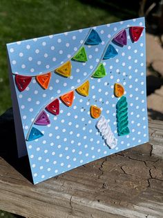 a birthday card with colorful candles and polka dots on blue paper, sitting on a wooden bench