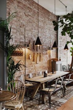 an instagramted photo of a dining room with brick walls and wooden tables, hanging lights, potted plants