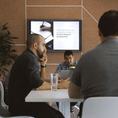 two men sitting at a table in front of a flat screen tv, talking to each other