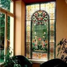 a stained glass window with flowers in the center and two chairs near it, next to a potted plant