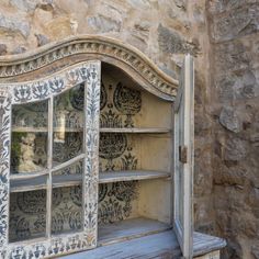 an old wooden cabinet with glass doors on it's sides, in front of a stone wall