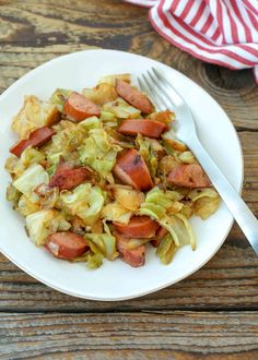 a white plate topped with cabbage and sausage next to a fork on a wooden table