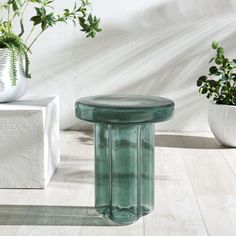 a green glass table sitting on top of a wooden floor next to potted plants