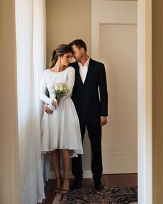 a man and woman in formal wear standing next to each other near a doorway, looking at each other