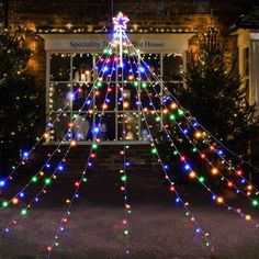 a christmas tree is decorated with multi - colored lights in front of a building at night