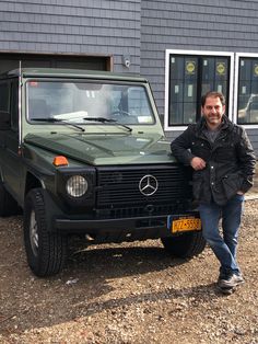 a man standing next to a green mercedes benz truck in front of a garage door