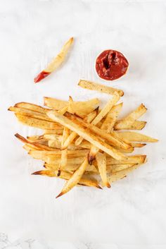 french fries with ketchup and mustard on a white tablecloth next to a small bowl of ketchup