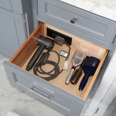 an open drawer with hairdryers, combs and other items in it on a marble countertop