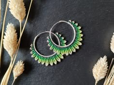 two green and white beaded hoop earrings sitting on top of some dry grass next to dried flowers