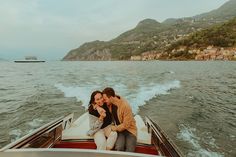 two people are sitting on the back of a boat in the water, one is kissing the other's head