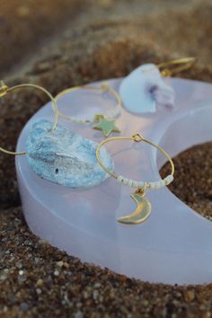 a pair of earrings sitting on top of a purple piece of glass in the sand