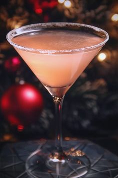 a close up of a drink in a glass near a christmas tree