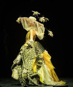 a woman in an elaborate dress with bees on her head and wings flying above her