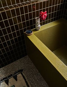 a bathroom with tiled walls and a yellow bathtub next to a vase with red flowers