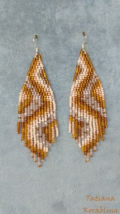 two pairs of beaded earrings with fringes on blue fabric, one in gold and the other in white