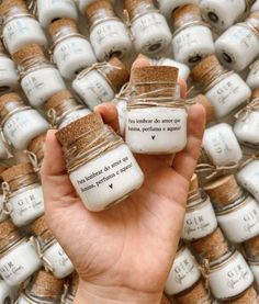 a person holding two small jars in front of a pile of smaller jars with writing on them