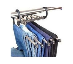 clothes hanging on a rack in front of a white wall with blue jeans and black pants