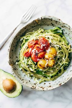 a white bowl filled with zucchini and tomatoes next to an avocado