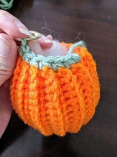 someone is crocheting the stitches on an orange pumpkin ornament with scissors