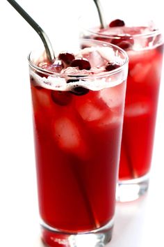 two glasses filled with ice and cherries on top of a white table next to each other