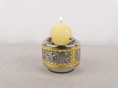 a yellow candle sitting in a silver and gold container