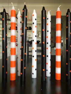 orange and white candles are lined up on a black table with an orange striped one