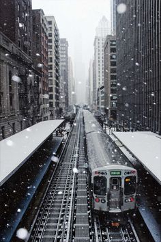 a train traveling down tracks in the middle of a snow covered city with tall buildings